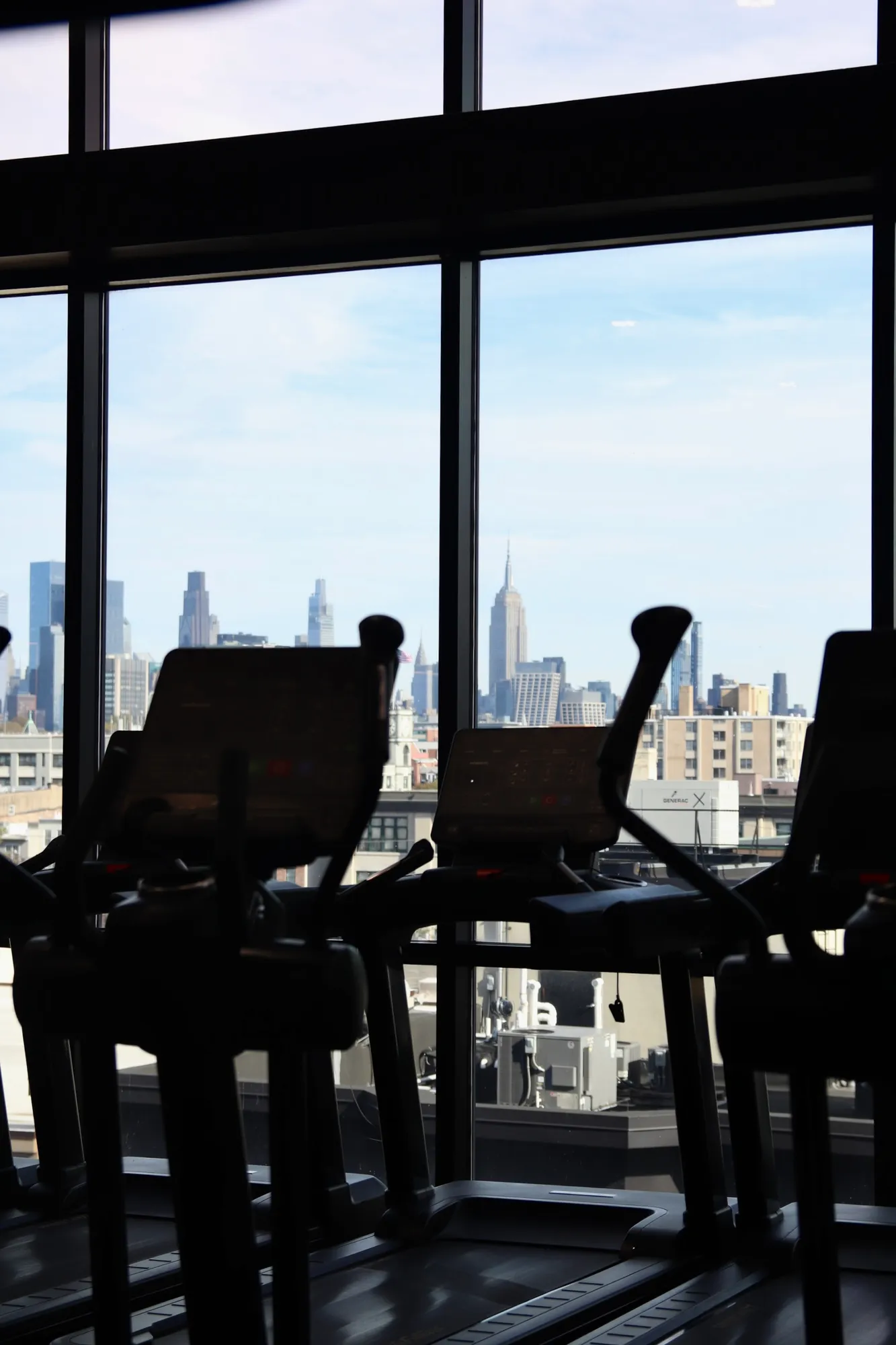 Treadmills silhouetted against the Manhattan skyline and Empire State Building at XCEL Athletic Lifestyle, a rooftop gym in Hoboken, NJ