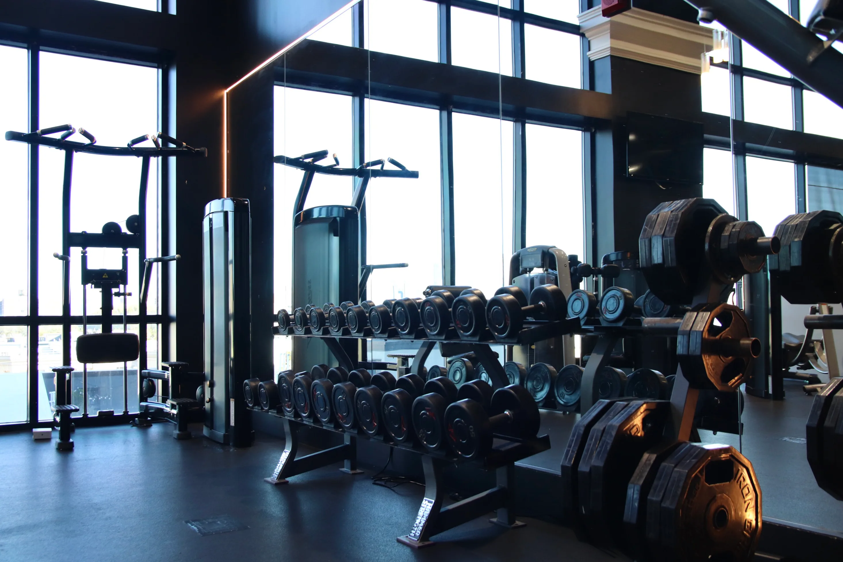 Dumbbell racks and pull-up stations by floor-to-ceiling windows at XCEL Athletic Lifestyle, a rooftop gym in Hoboken, NJ