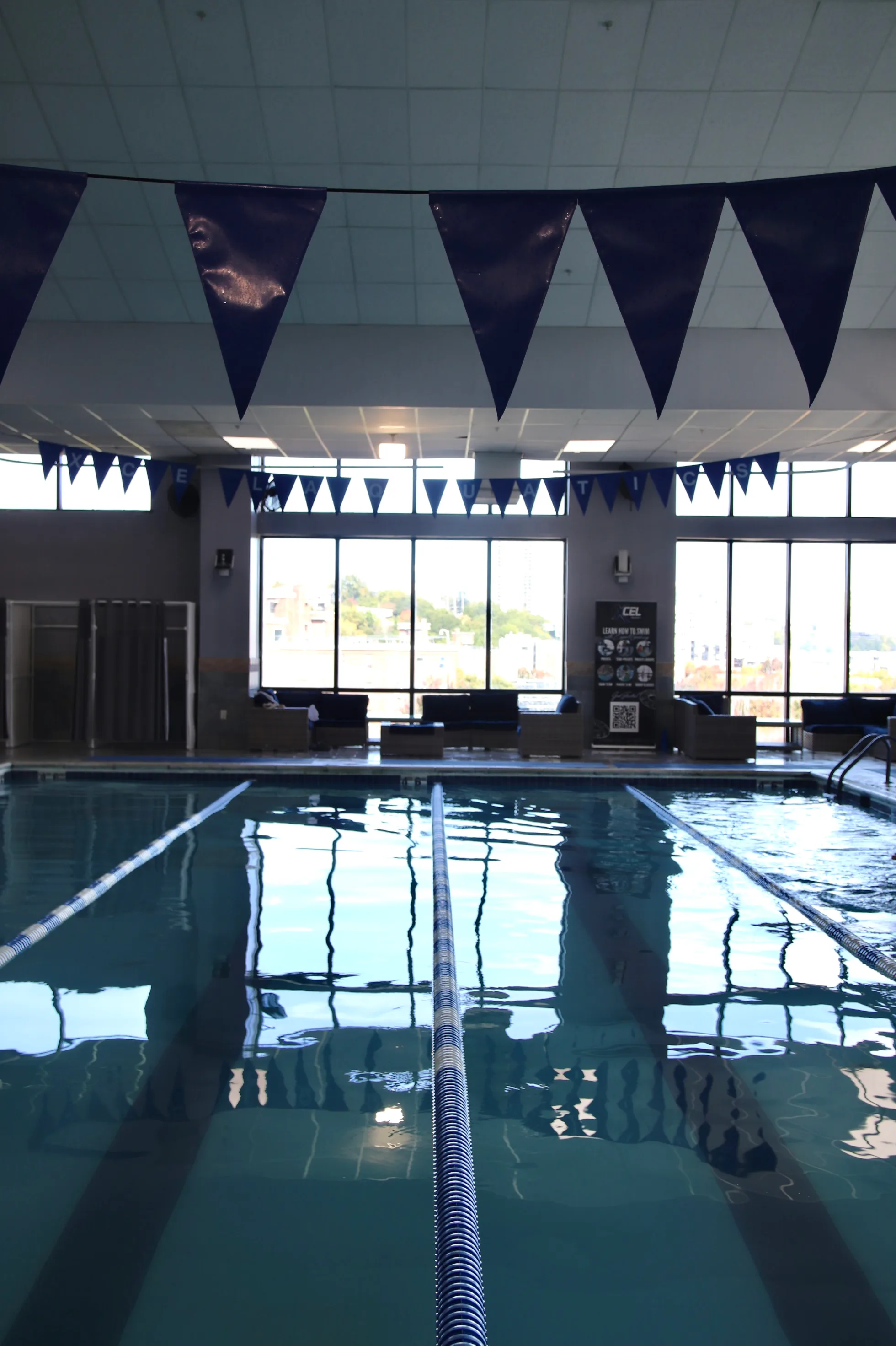 Heated indoor lap pool with swim flags overhead at XCEL Athletic Lifestyle, a rooftop gym in Hoboken, NJ