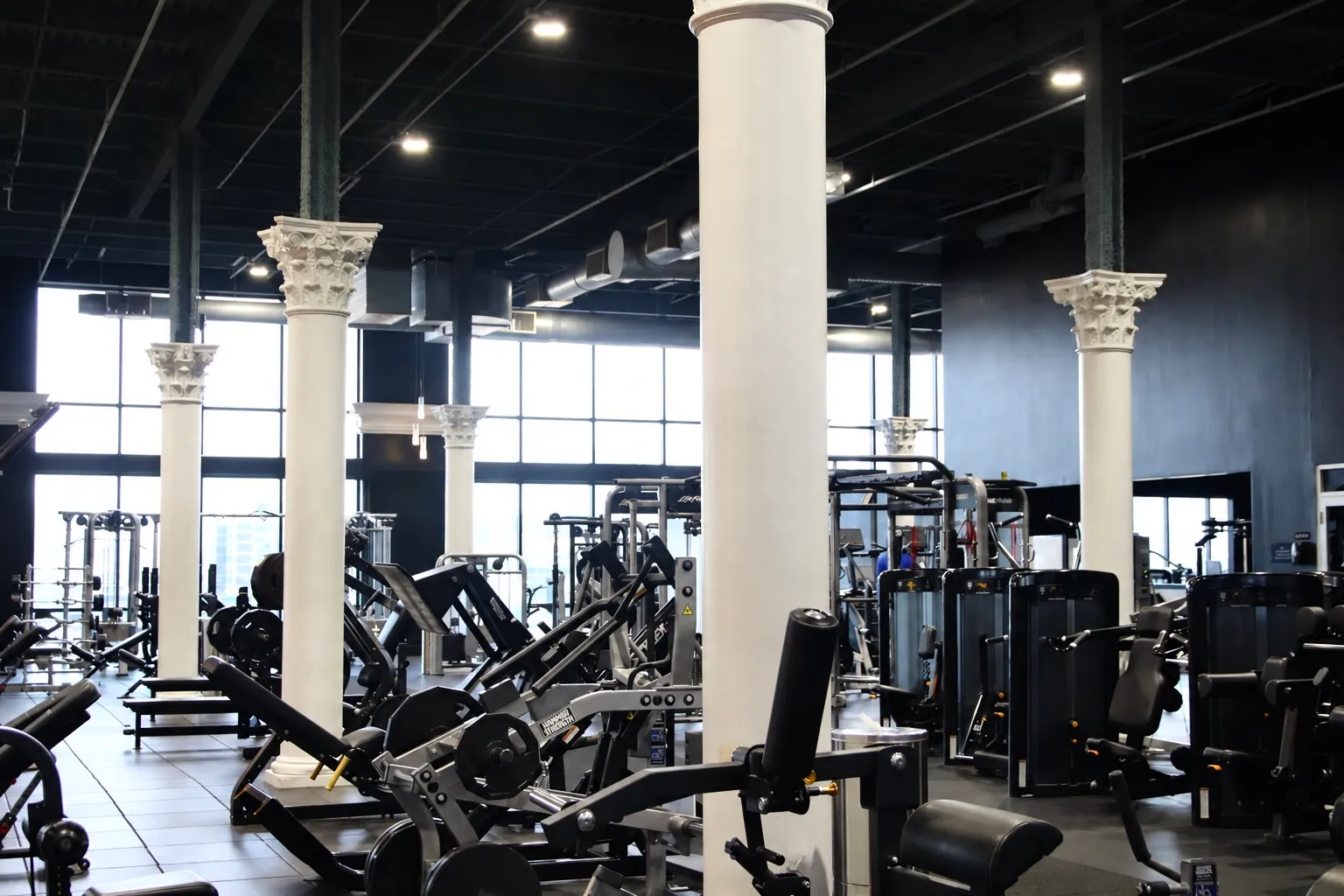 Bright strength floor full of machines between white columns at XCEL Athletic Lifestyle, a rooftop gym in Hoboken, NJ