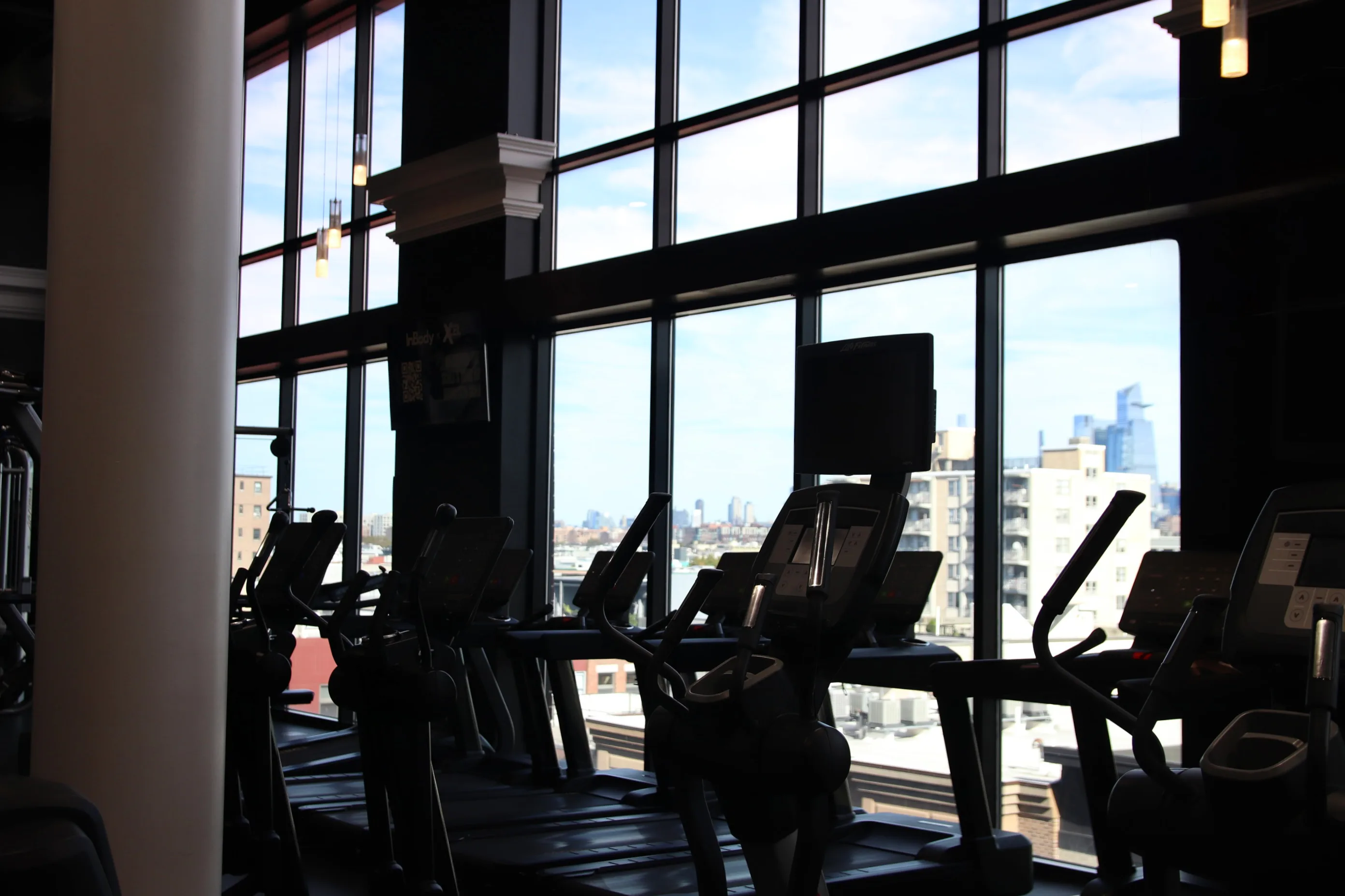 Treadmills and ellipticals facing the skyline at XCEL Athletic Lifestyle, a rooftop gym in Hoboken, NJ