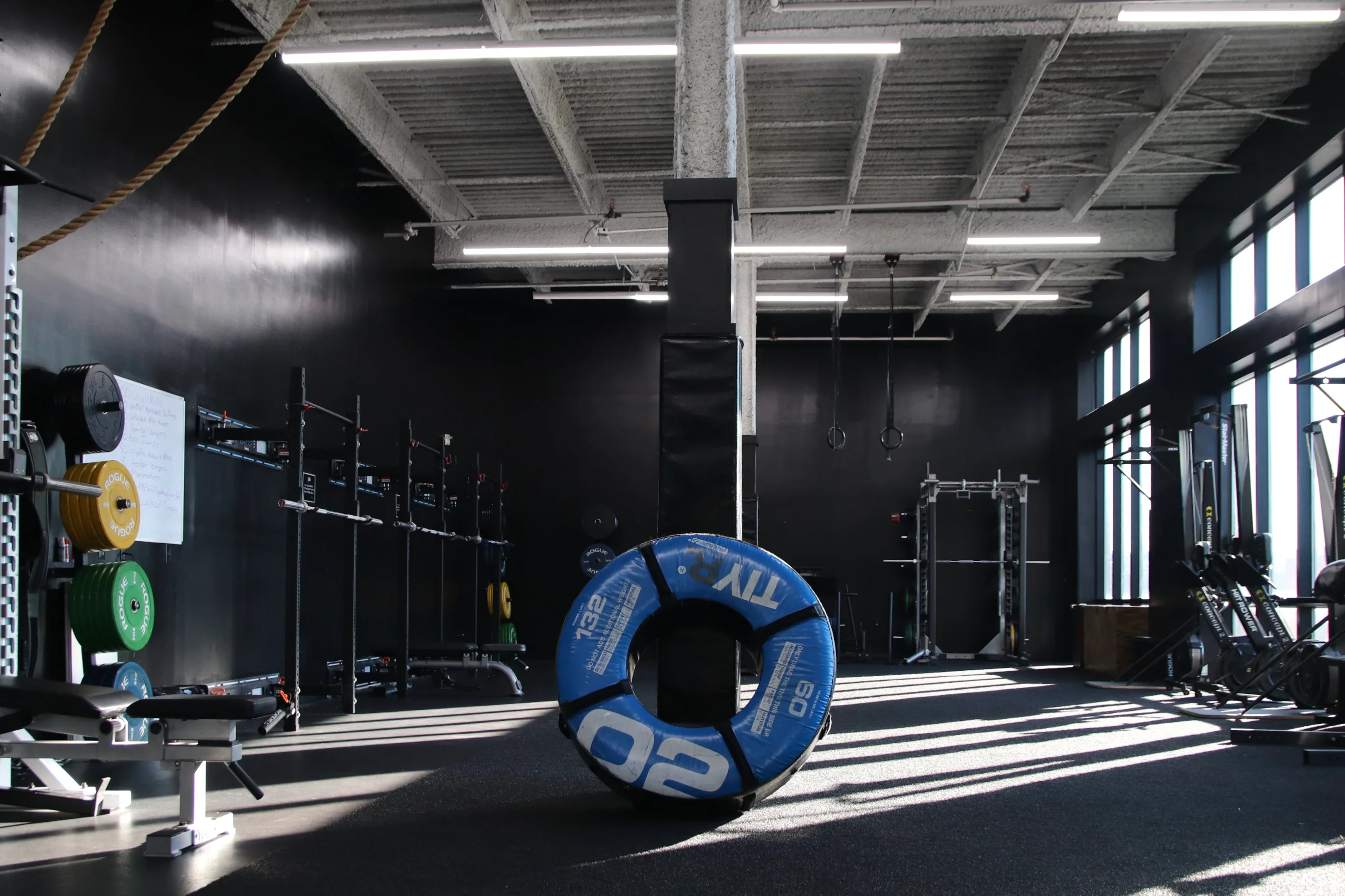 Sunlit functional training area with racks and a training tire at XCEL Athletic Lifestyle, a rooftop gym in Hoboken, NJ